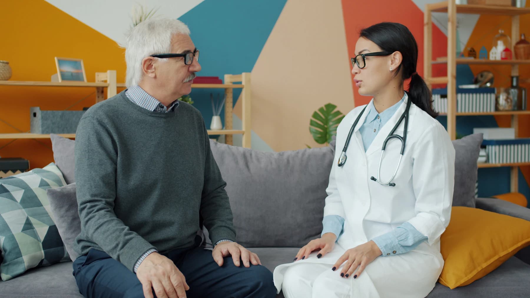 A clinician and an older patient in conversation on a couch during an illustrative visit